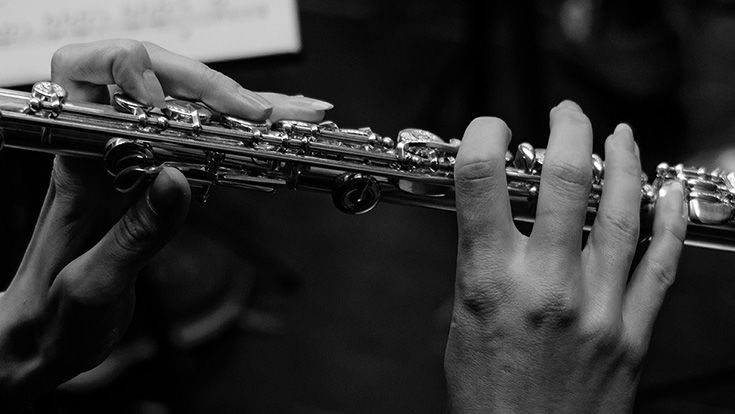 Hands playing a flute against a black background