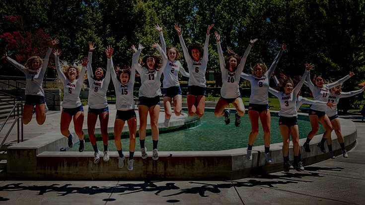 Dimmly-lit photo of volleyball players jumping